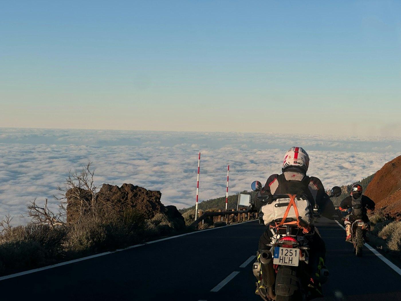 Two riders on a road above a sea of clouds
