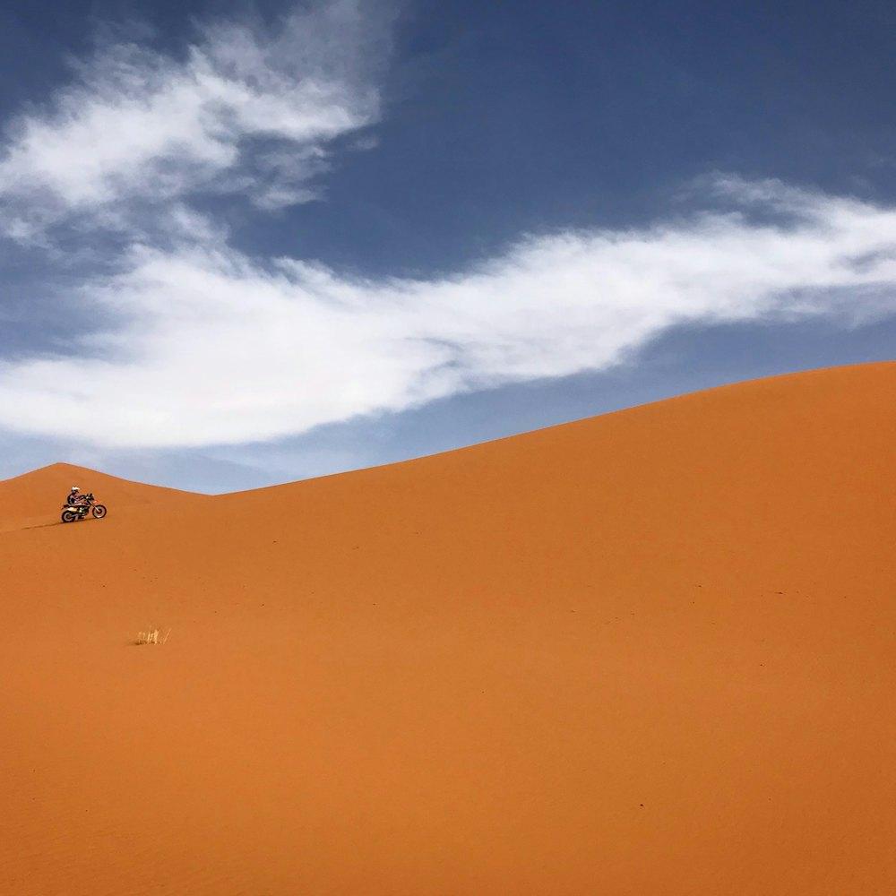 Tiny rider crossing huge orange sand dunes